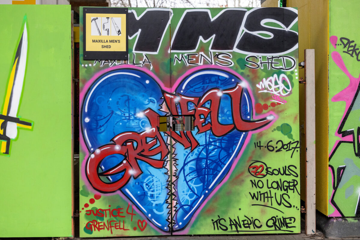 Street view close-up of the Shed's entrance, depicting wooden gates adorned by bright graffiti artwork dedicated to the 72 lives lost at Grenfell Tower.