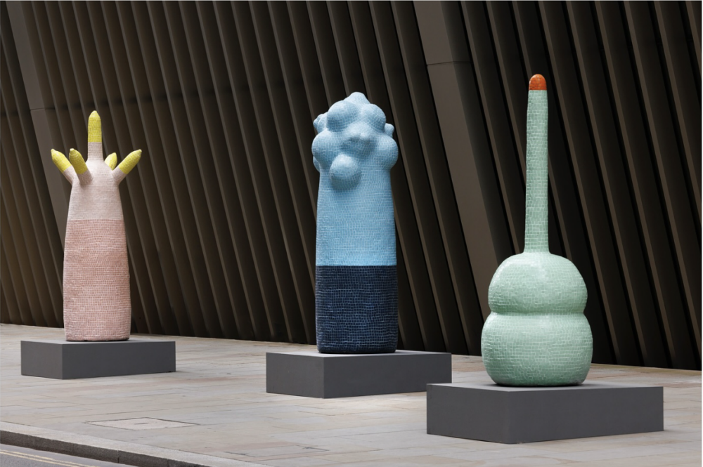 Photograph of three large totemic and blobby sculptures in pastel colours installed outdoors on a modern street.